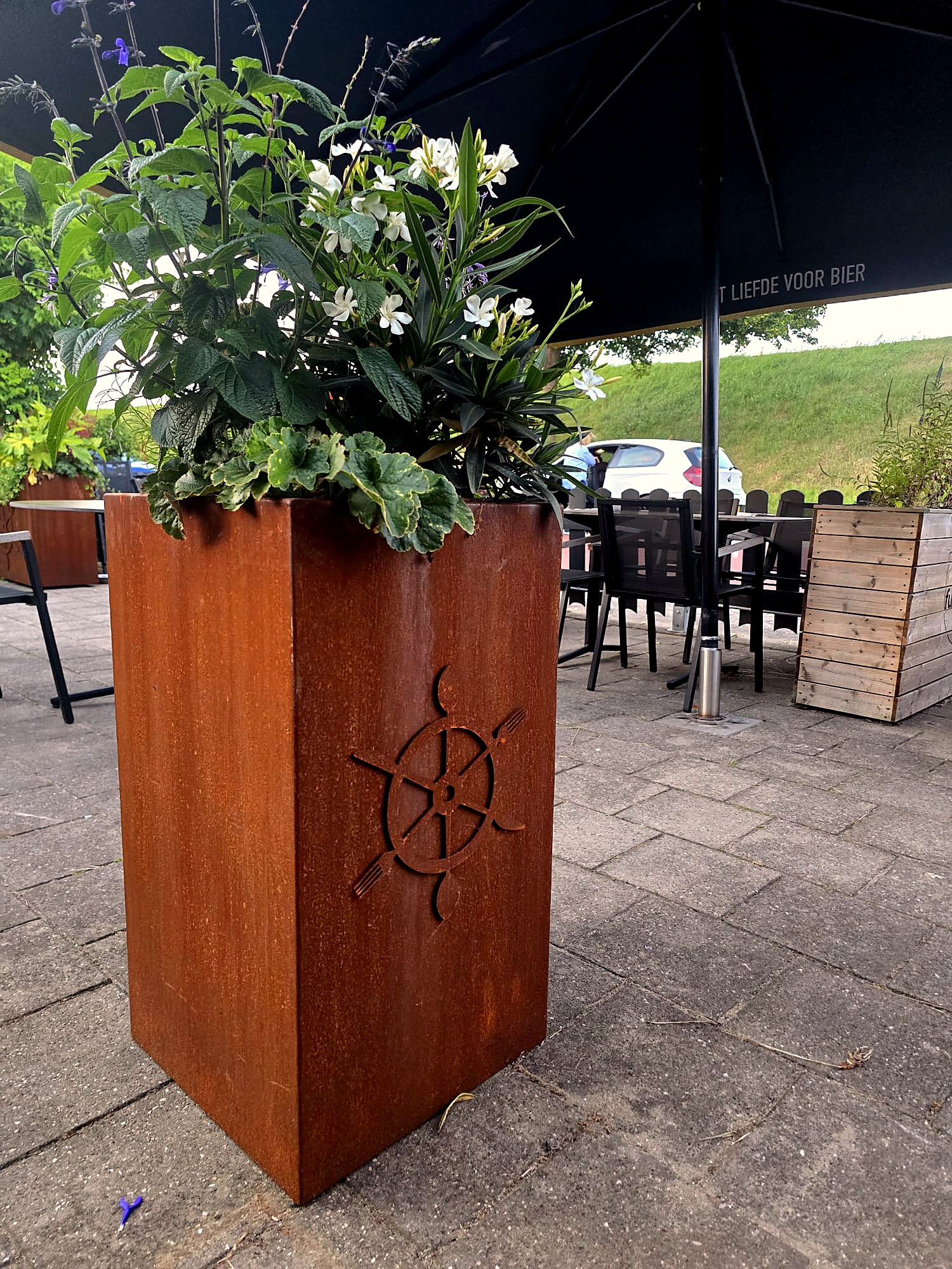 Hoge cortenstalen plantenbak met uitgesneden logo op het terras van Hotel Brasserie Smits